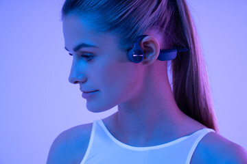 Beautiful woman in neon light wearing sport bone conduction headphones during fitness workout