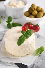 Ricotta cheese. Homemade Ricotta cheese with basil, garlic, tomatoes and green olives on parchment paperback and stand on old beige tiles background. Italian food.  Selective focus.