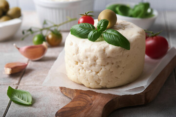 Ricotta cheese. Homemade Ricotta cheese with basil, garlic, tomatoes and green olives on parchment paperback and stand on old beige tiles background. Italian food.  Selective focus.