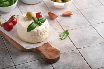 Ricotta cheese. Homemade Ricotta cheese with basil, garlic, tomatoes and green olives on parchment paperback and stand on old beige tiles background. Italian food.  Selective focus.