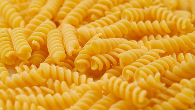 Background Of Fusilli Pasta. Uncooked Italian Pasta Golden Rotating Backdrop. Healthy Eating Concept. Raw Dried Organic Pasta. Spiral Macaroni, Rotating Background. Italian Culture and Cuisine Pattern