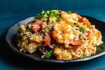 Fried rice with bacon and shrimp against a blue plaster design board. 