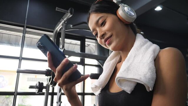 Fitness relaxing concept. Young sporty woman listening to music on smartphone in gym, break after hard workout. 4k resolution.