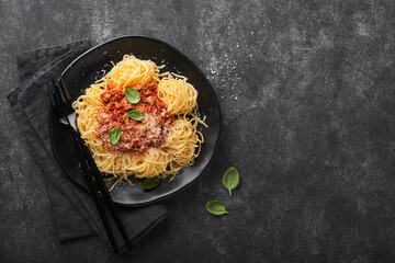 Classic spaghetti pasta Bolognese. Tasty appetizing italian spaghetti with bolognese sauce, tomato sauce, cheese parmesan and basil on black plate on dark stone or concrete table background. Top view.