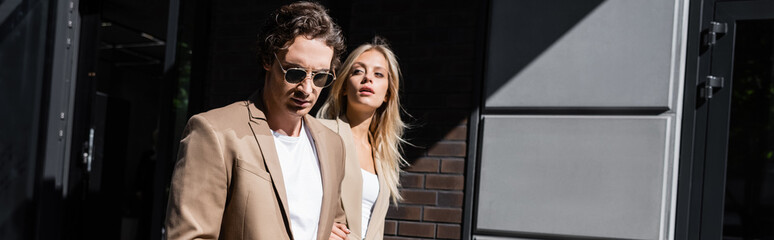 pretty blonde woman looking away near man in sunglasses outdoors, banner.