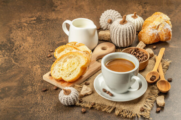 Breakfast concept with a cup of coffee, croissants, milk jug, and decorative crochet pumpkins