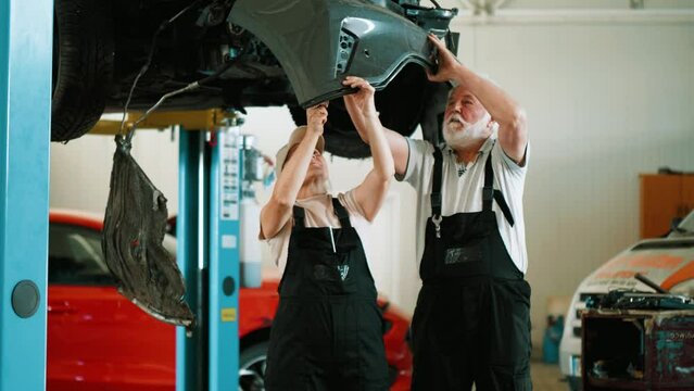 Two employed mechanics in the workshop remove damaged parts from a crashed car after a collision in the workshop