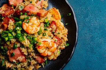 Fried rice with bacon and shrimp against a blue plaster design board. 