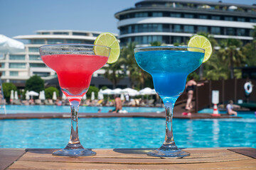 Cocktails by the pool. Red and blue cocktail on a wooden table, on vacation