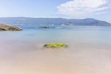 Isolated rock on the desert beach with clouds and blue sky.