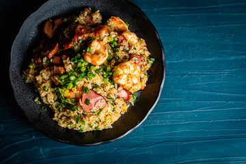 Fried rice with bacon and shrimp against a blue plaster design board. 