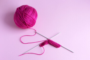 Pink knitted wool on a pink background with knitting needles, hobby