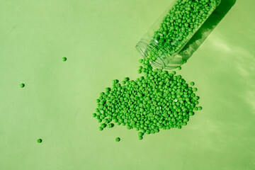 GRANULES OF GREEN WAX LIE ON A GREEN BACKGROUND, POURED FROM A TRANSPARENT JAR. SPACE FOR TEXT