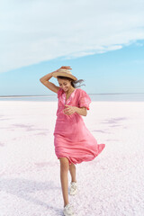 Elegant fabulous woman walking by salt flats beach of pink lake against blue sky. Girl in hat and...