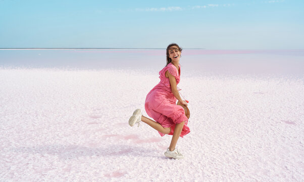 Motion image of joyful laughing woman dancing or running in pink dress on desert beach of salt pink lake.