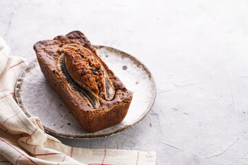 Chocolate banana bread with walnuts on a white plate with brown rim on a grey neutral background , space for text