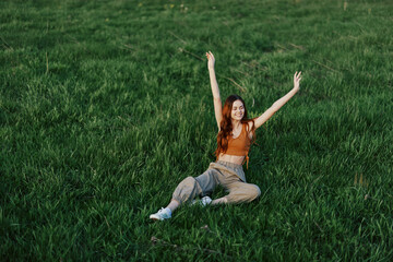 A young woman playing games in the park on the green grass spreading her arms and legs in different directions falling and smiling in the summer sunlight