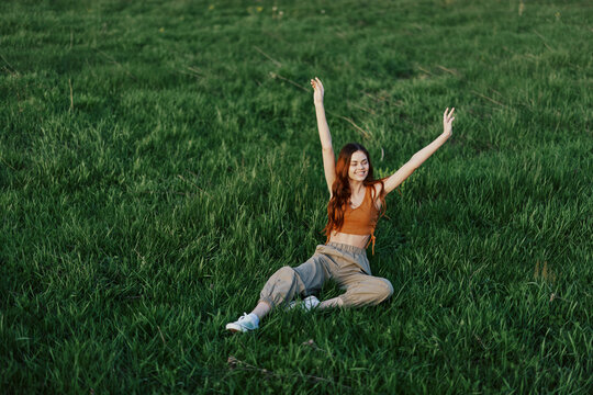 A Young Woman Playing Games In The Park On The Green Grass Spreading Her Arms And Legs In Different Directions Falling And Smiling In The Summer Sunlight