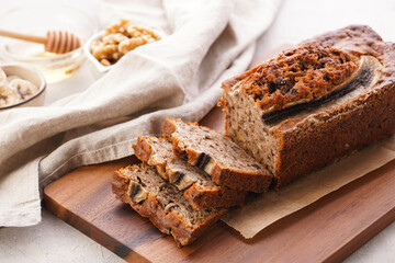 Chocolate banana bread with walnuts on a wooden board and ingredients on a grey neutral background