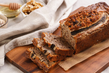 Chocolate banana bread with walnuts on a wooden board and ingredients on a grey neutral background