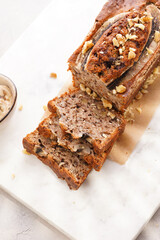 Chocolate banana bread with walnuts on a marble board and ingredients on a grey neutral background