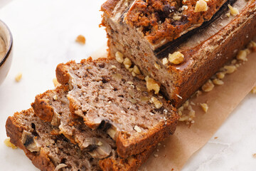 Chocolate banana bread with walnuts on a marble board and ingredients on a grey neutral background