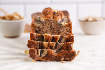 Slices of Chocolate banana bread with walnuts on a marble board and ingredients on a grey neutral background