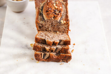 Slices of Chocolate banana bread with walnuts on a marble board and ingredients on a grey neutral background with creative lighting