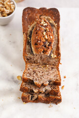 Slices of Chocolate banana bread with walnuts on a marble board and ingredients on a grey neutral background