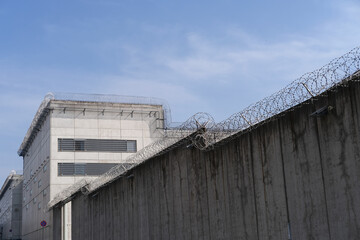 high concrete fence, barbed wire fence on top, pre-trial detention cell, building for execution of...