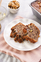 Slices of Chocolate banana bread with walnuts on a pink kitchen napkin and ingredients on a grey neutral background with creative lighting
