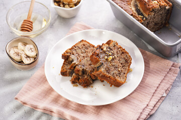 Slices of Chocolate banana bread with walnuts on a pink kitchen napkin and ingredients on a grey neutral background with creative lighting