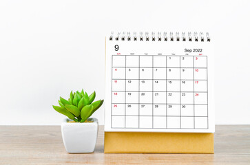 September 2022 desk calendar with plant on wooden table.