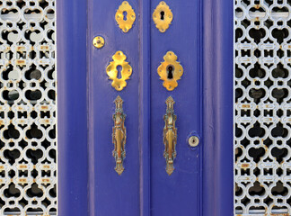 Blue wooden door and iron bars on the sides. An old door with carved handles and an exterior lock. 