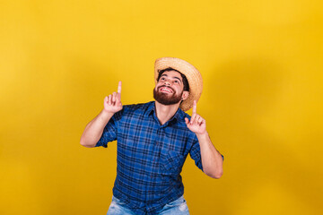 Bearded man, wearing typical clothes for the Festa Junina. Feast of Arraiá de São João. pointing up with your fingers. - obrazy, fototapety, plakaty