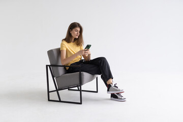 Young woman with smartphone sitting in armchair isolatedon white background