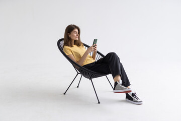 Young woman with smartphone sitting in armchair isolatedon white background
