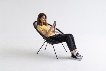 Young woman with smartphone sitting in armchair isolated on white background