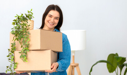 Smiling pretty caucasian woman standing in her new flat with a stack of cardboard boxes and...