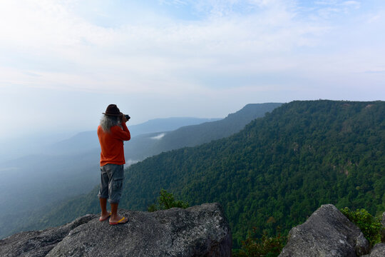 Photographer takes photos of the landscape on  top of the rock mountain at In the morning and light fog in the middle of the perfect natural forest background