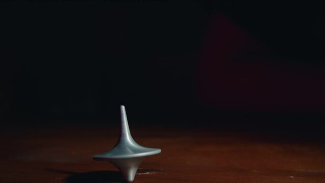 Hand playing with a top spinning on a wooden table in slow motion