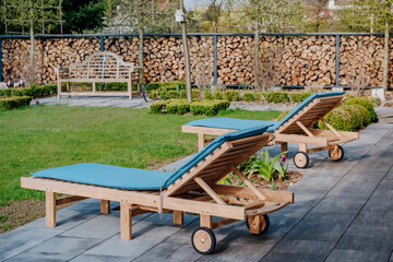 Sun loungers on the terrace in the green garden with a wooden bench. A place of rest and relaxation in the garden - obrazy, fototapety, plakaty