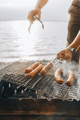 Close up unrecognizable man hands smoked pork meat on outdoor barbecue. Chef putting juicy sausage...