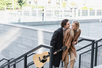 young man with acoustic guitar and stylish blonde woman walking in city.