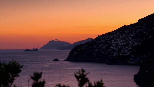 Timelapse video of sunset on the Amalfi Coast with the small town of Praiano on the left and the island of Capri far away on the horizon.