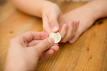 Adult giving coin to a child as saving money concept. Children's financial education, financial literacy. Payment for duties performed.