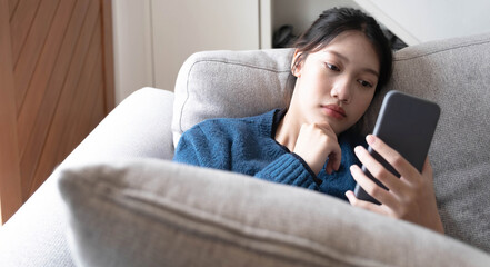 Asian lay on couch in living room frustrated with slow Internet connection or spam on smartphone.
