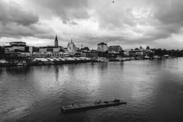 Panoramic view of Valdivia riverbank and marketplace ("Mercado Fluvial") with Calle-calle river with sea lions, birds, boats and ships and cloudy sky, Chile (in black and white)