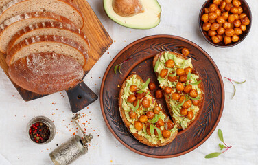 Healthy vegan and vegetarian rye bread sandwiches with avocado, chickpeas, spices and microgins (green shoots). Delicious gourmet breakfast in a clay plate. Selective focus, top view