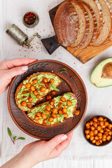 Healthy vegan and vegetarian rye bread sandwiches with avocado, chickpeas, spices and microgins (green shoots). Delicious gourmet breakfast in a clay plate. Selective focus, top view